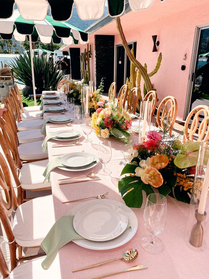 a long table set with plates and place settings for an outdoor dinner or brunch