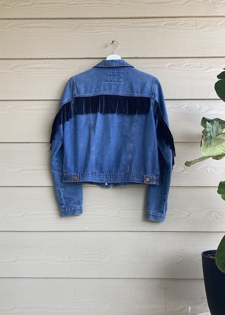 "This is a secondhand, one-of-a-kind denim jacket with a handmade zero-waste fringe sewn onto the back and sleeves, making this item completely secondhand and unique! Features button closure and front pockets. Spot treat, or wash inside out and lay flat to dry. Listed size is a Small but more accurately fits up to a smaller Medium; modeled on a size Small. Measurements when buttoned- Bust: 38\" Hip: 36\" Length: 20 1/2\" **This product helps to minimize textile waste in the fashion industry by using only secondhand materials, some unfit for resale. Due to the item's secondhand nature, there may be light signs of wear. Bottom button has been repaired. Repairs are covered by The Uncommon Closet for the lifespan of the garment." Bohemian Denim Jacket With Frayed Hem, Fringe Denim Jacket In Medium Wash, Fringe Cotton Denim Jacket For Fall, Fall Cotton Denim Jacket With Fringe, Fall Fringe Cotton Denim Jacket, Long Sleeve Cotton Denim Jacket With Fringe, Casual Medium Wash Denim Jacket With Fringe, Cotton Denim Jacket With Fringe, Fitted Fringe Denim Jacket Casual