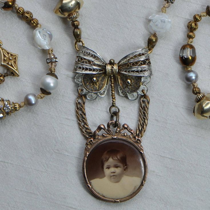 * Le Bébé - one of a kind, antiques assemblage necklace, handmade by moi * Antique photograph of a French baby girl set in 12kt gold filled frame * 800 silver filigree bow * Beads, knotted on silk cord include the following materials: * Carved mother of pearl roses, vermeil (18kt gold covered sterling silver), crystal, brass, white and grey cultured pearls * Vermeil hook and eye clasp * 22 3/4 inches (58 cm) long around the neck * I design and construct my pieces to become heirlooms and with car Elegant Antique Gold Jewelry For Memorial, Heirloom Memorial Pendant Necklace, Antique Gold Elegant Jewelry For Memorial, Elegant Vintage Charm Necklace For Memorial, Victorian Pendant Necklace For Vintage Events, Victorian Antique Silver Round Pendant Necklace, Victorian Antique Silver Necklace With Round Pendant, Victorian Pendant Necklace With Antique Finish, Handmade Bronze Necklaces For Wedding