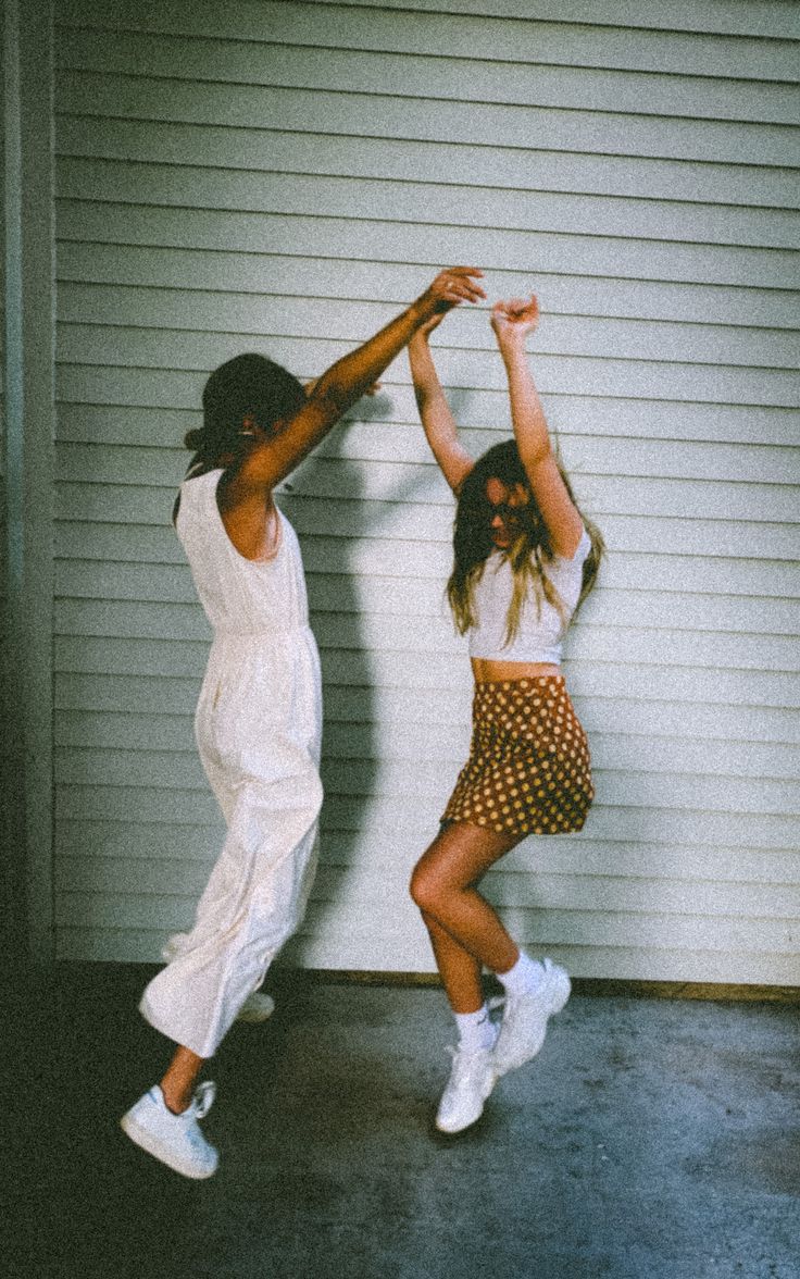 two young women are dancing in front of a garage door with their arms up to each other