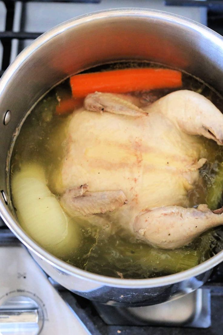 a chicken is cooking in a pot on the stove with carrots and broth