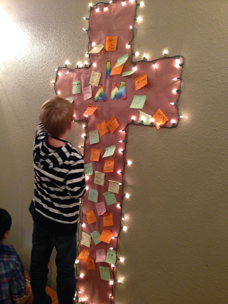 a young boy standing in front of a cross made out of post - it notes