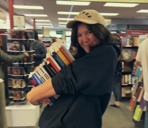 a woman holding a stack of books in a store