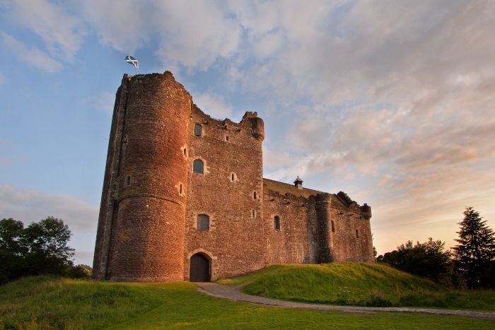 an old castle with a path leading to it on a grassy hill under a cloudy sky