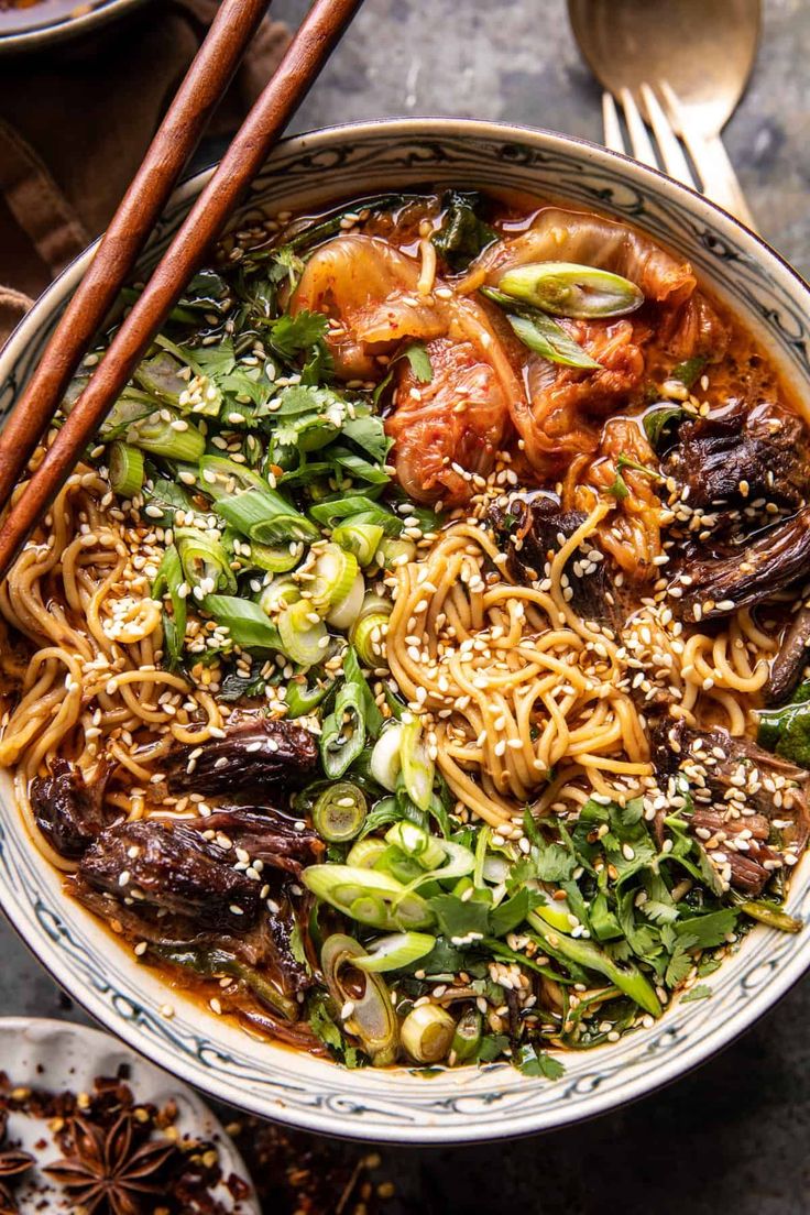 a bowl filled with noodles and vegetables next to chopsticks on top of a table