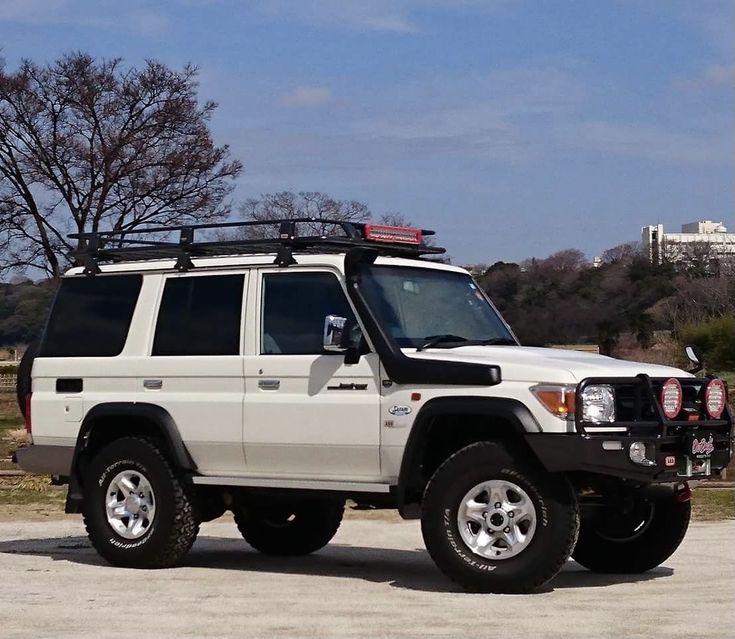 a white four door suv parked on top of a parking lot next to a tree