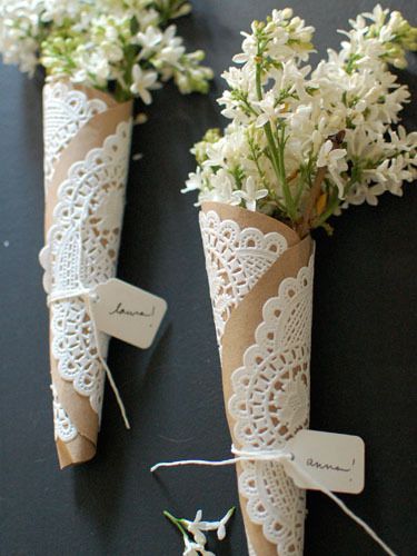 two vases with flowers tied to them on a black surface, one is made out of paper and the other has lace