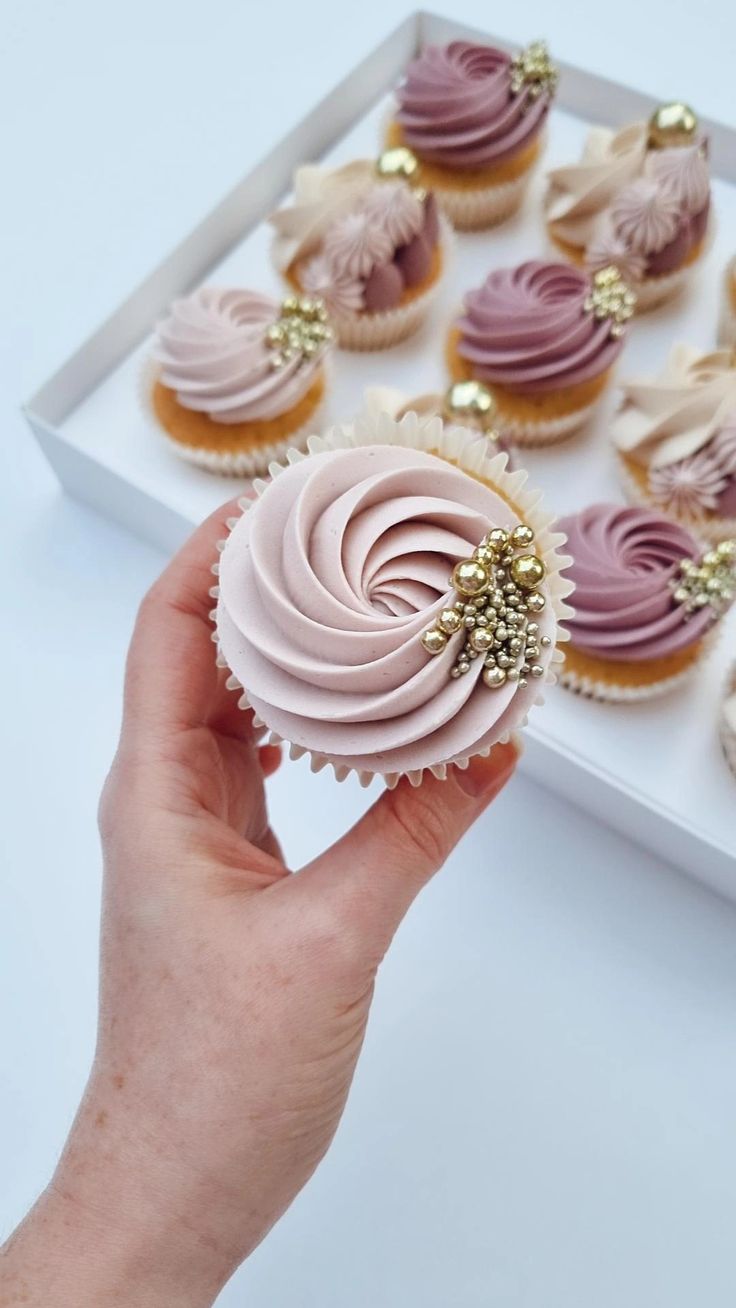 a hand holding a cupcake with pink frosting and gold sprinkles