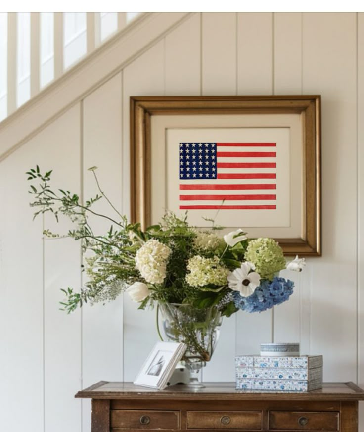 a vase filled with flowers sitting on top of a table next to a framed american flag