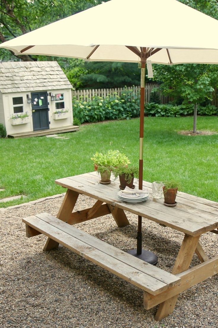 a picnic table with an umbrella and potted plants in the back yard on gravel