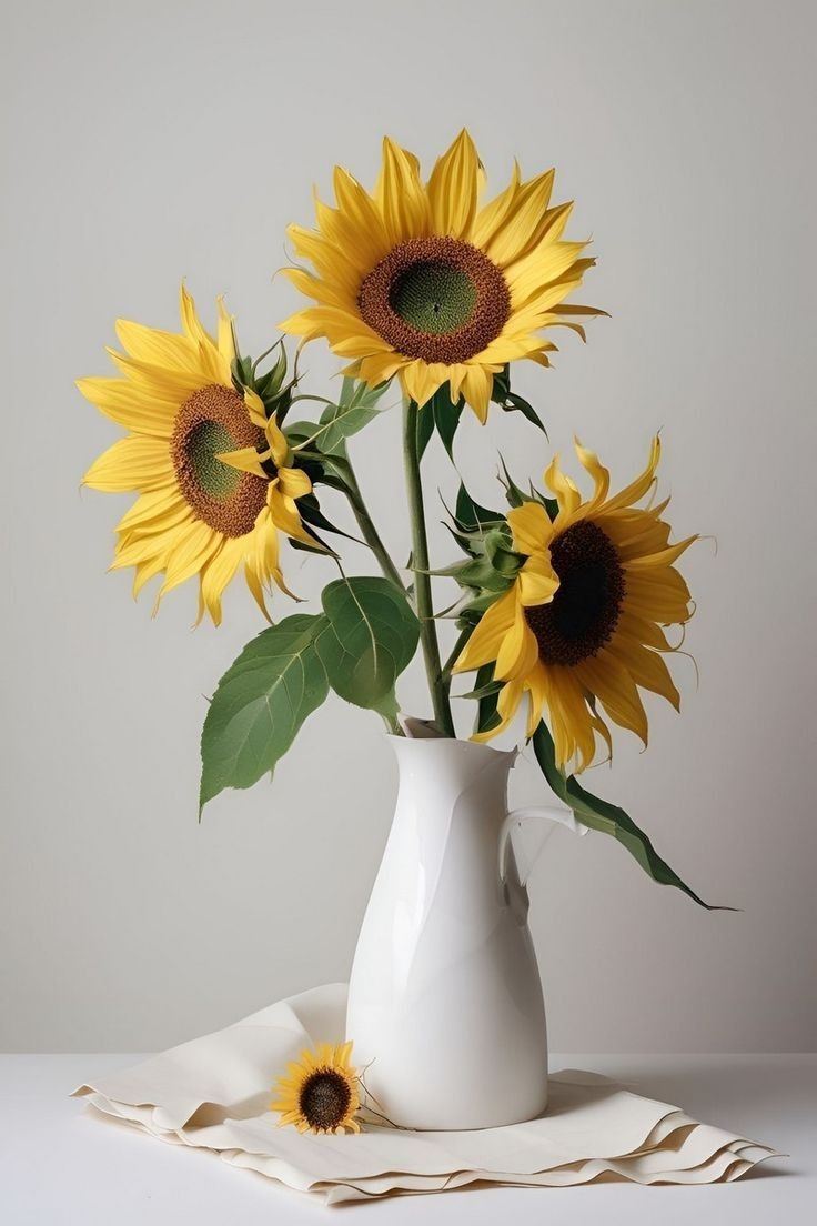 a white vase filled with yellow sunflowers sitting on top of a cloth covered table