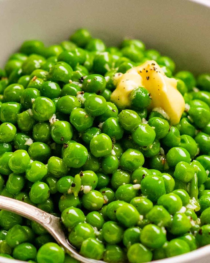 a bowl filled with green peas and topped with a buttered piece of cheese on top