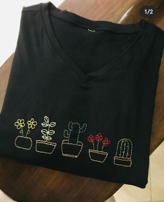 a black t - shirt with flowers and cacti embroidered on the front, sitting on a wooden table