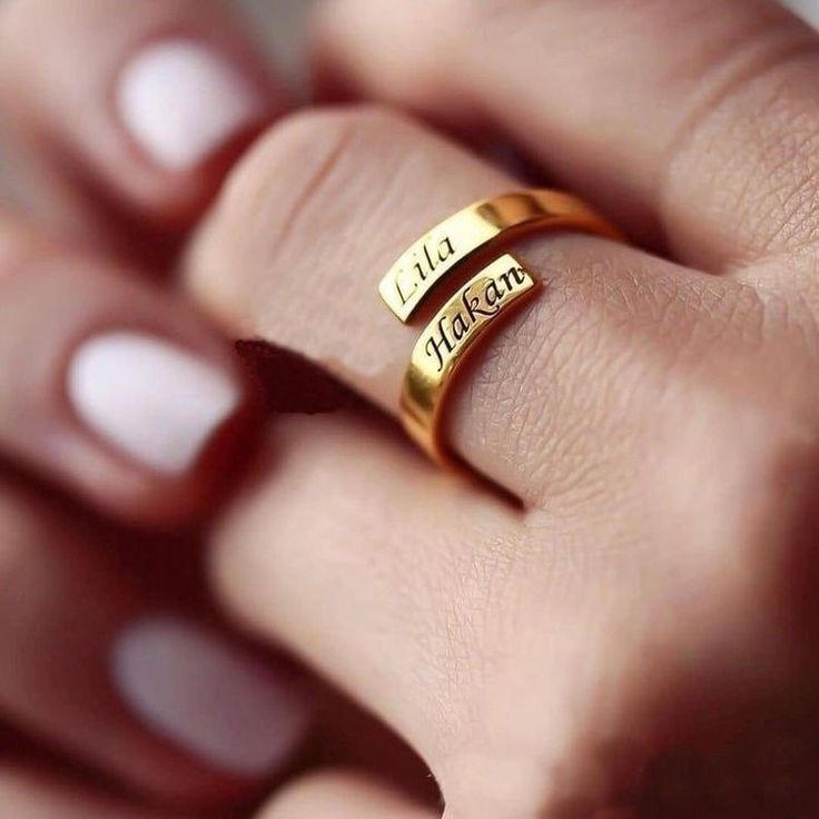 a woman's hand wearing a gold ring with two names engraved on the side