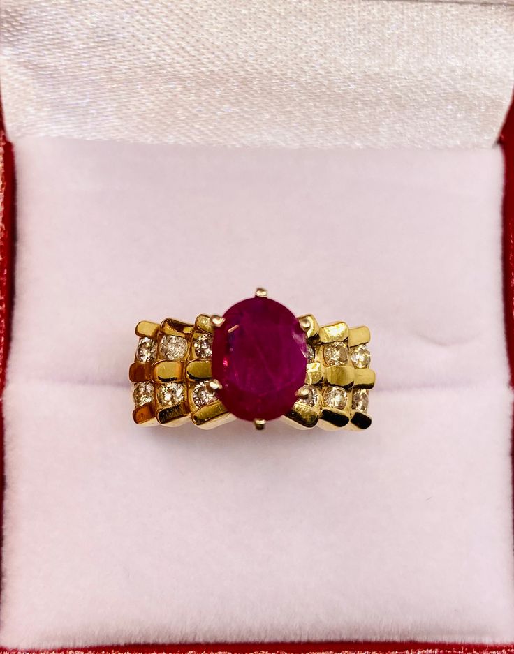 a red stone ring sitting on top of a white cloth covered cushion in a box