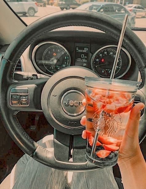 a person holding a drink in their hand while sitting in the driver's seat of a car