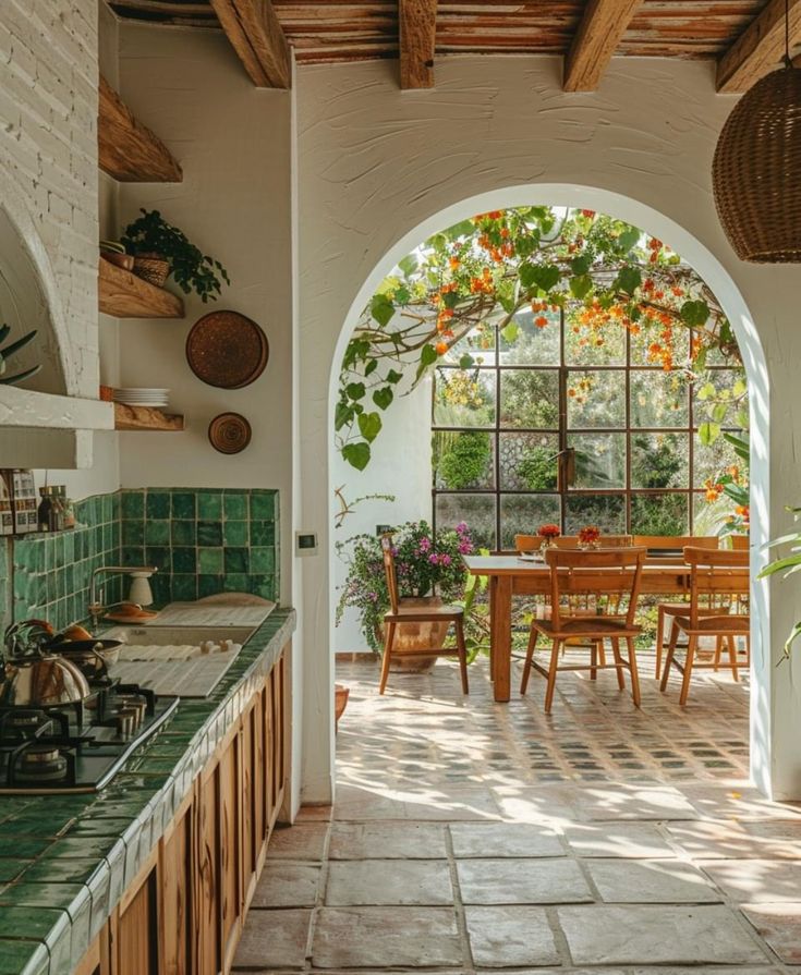 an arched doorway leads into a kitchen with green tile and wood furniture, along with potted plants on the counter