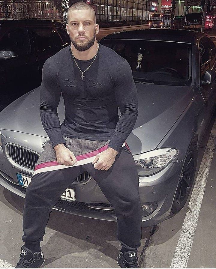 a man sitting on the hood of a car in front of a black sports car