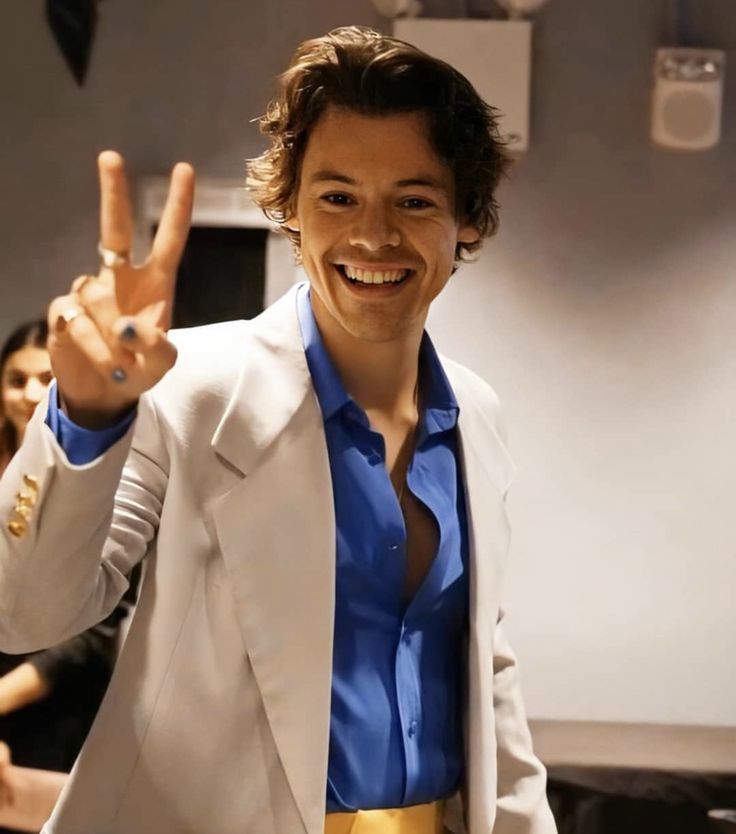 a man in a white suit and blue shirt making the peace sign with his hand