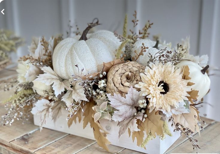 an arrangement of flowers and pumpkins in a white vase on a wooden table top