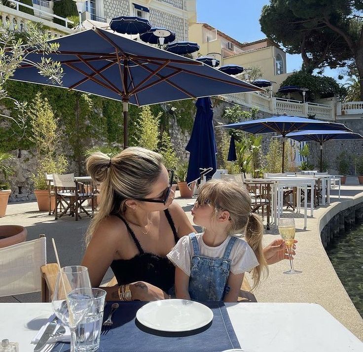 a woman and her daughter sitting at an outdoor table with drinks in front of them