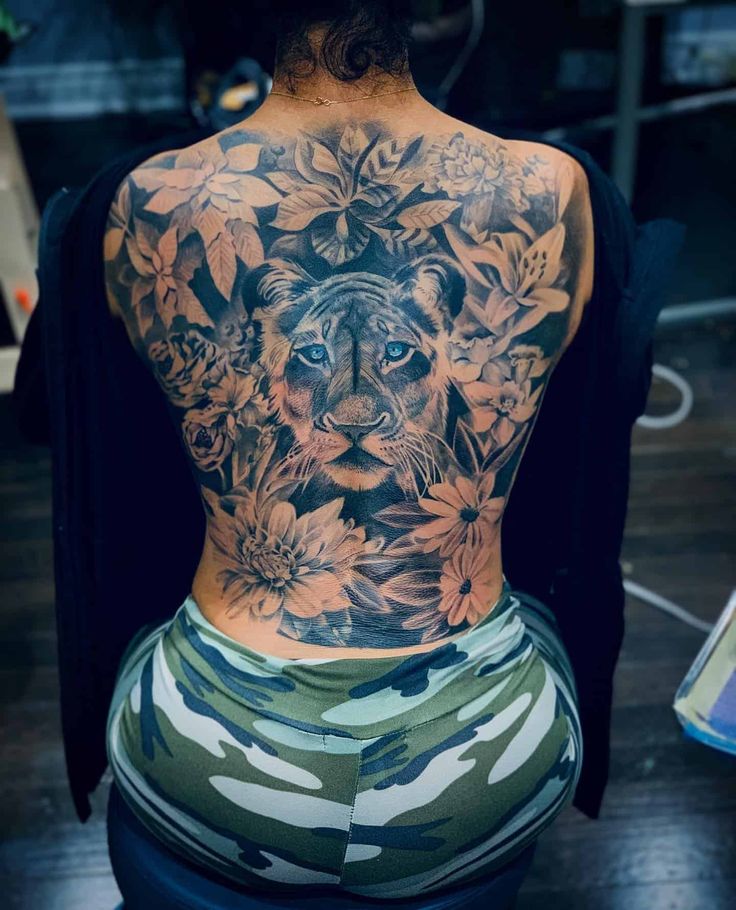 the back of a woman's body with flowers and a tiger tattoo on it