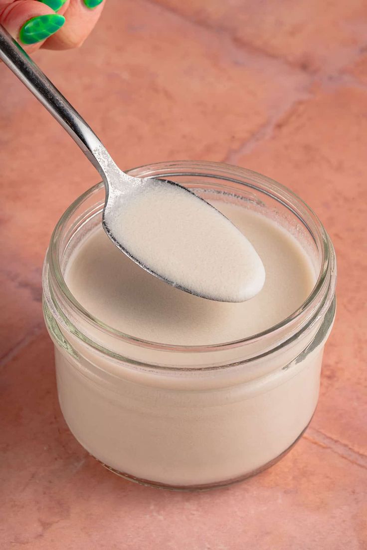 a spoon full of cream sitting on top of a pink tile floor next to a jar