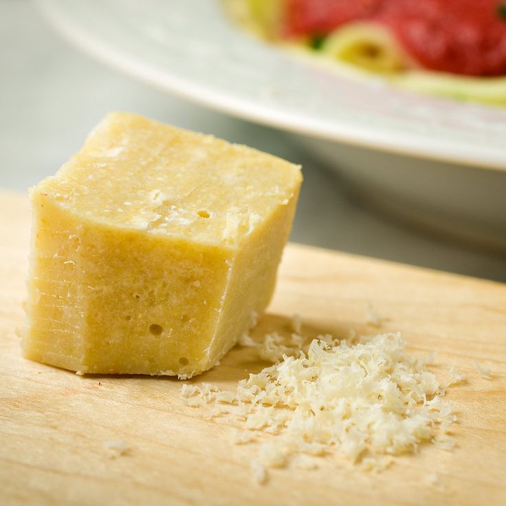 a piece of cheese sitting on top of a wooden cutting board next to a bowl