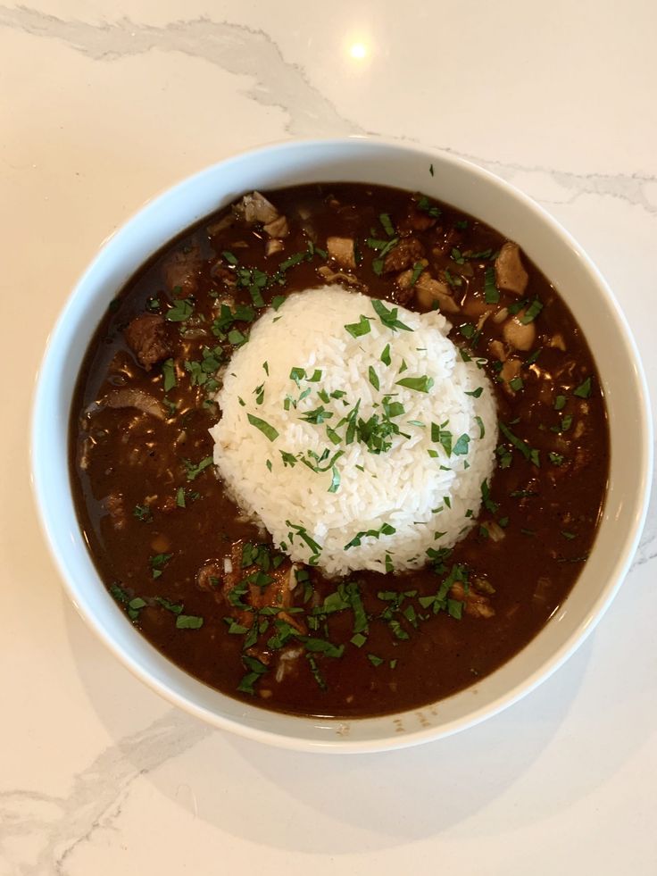 a white bowl filled with stew and rice on top of a table next to a spoon