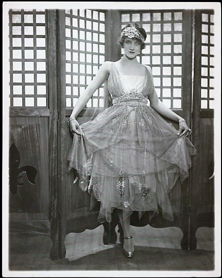 an old fashion photo of a woman in a dress and headdress posing for the camera