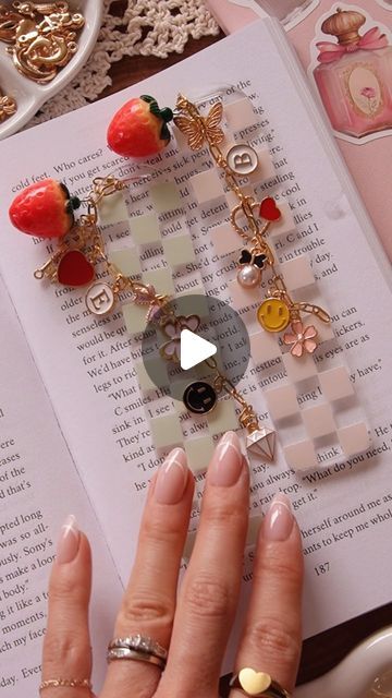 a woman's hands holding onto an open book with charms and fruit on it