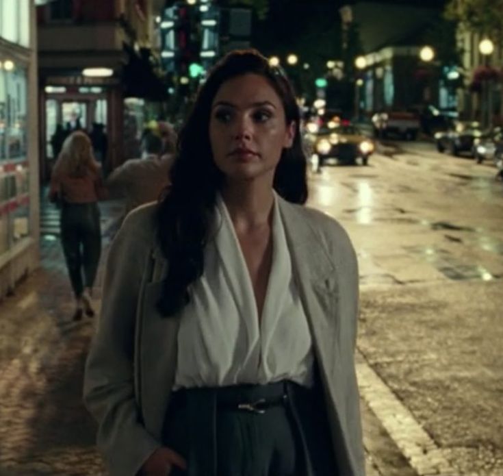 a woman standing in the middle of a street at night with her hands in her pockets