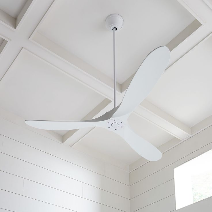 a white ceiling fan hanging from the ceiling in a room with white walls and wood paneling