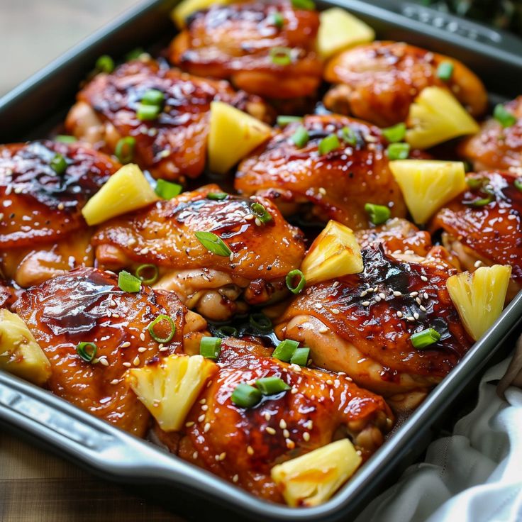 a pan filled with chicken and pineapples on top of a wooden table next to a white towel