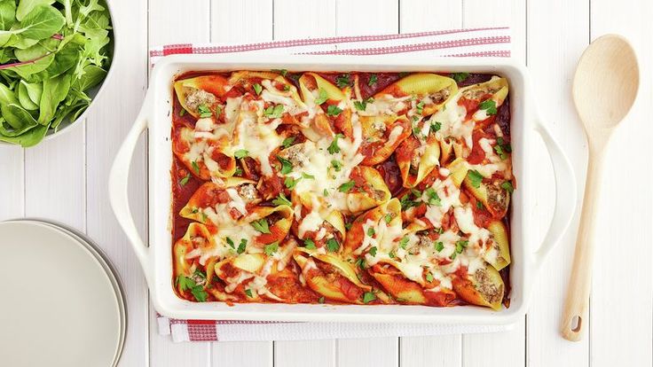 a casserole dish with meat, cheese and vegetables in it next to a salad