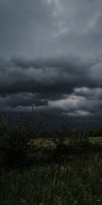 the sky is filled with dark clouds and green grass