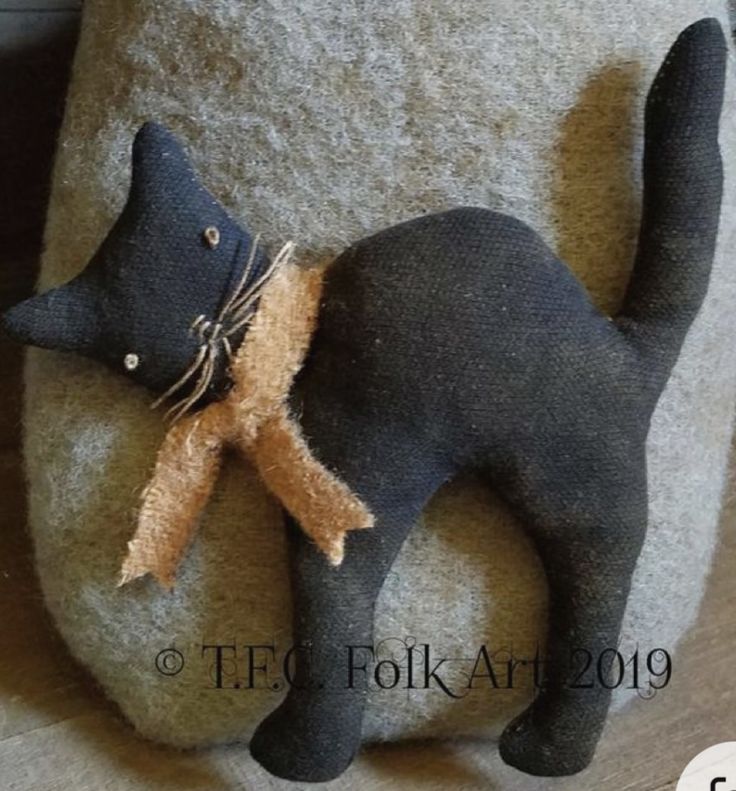 a black cat sitting on top of a gray pillow with a brown ribbon around it's neck