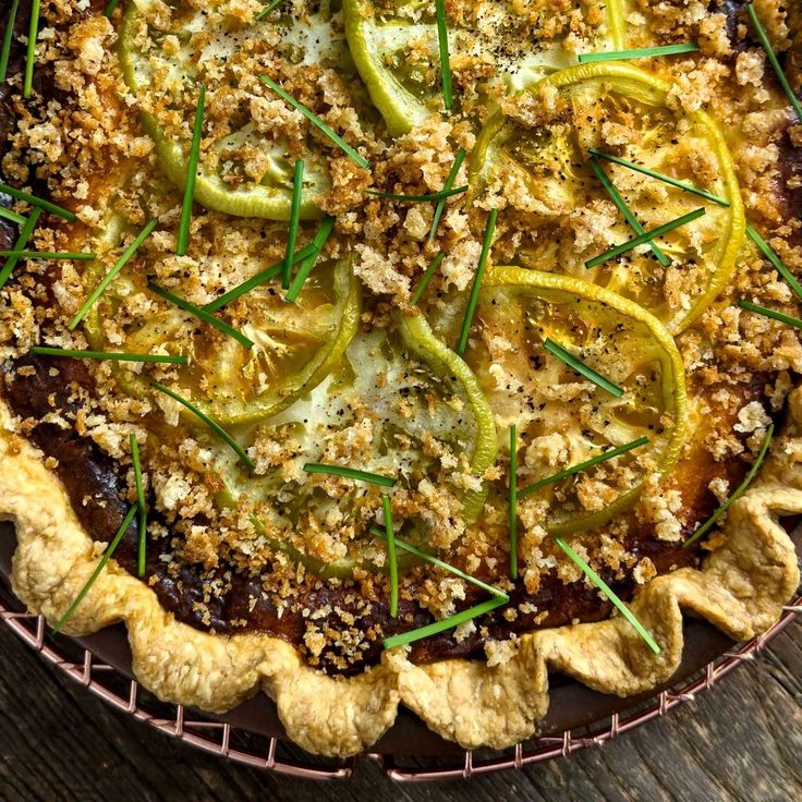 a pie topped with sliced green onions and cheese on top of a wooden table next to a fork