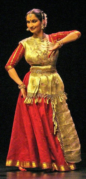 a woman in a red and gold dress standing on a stage with her arms outstretched