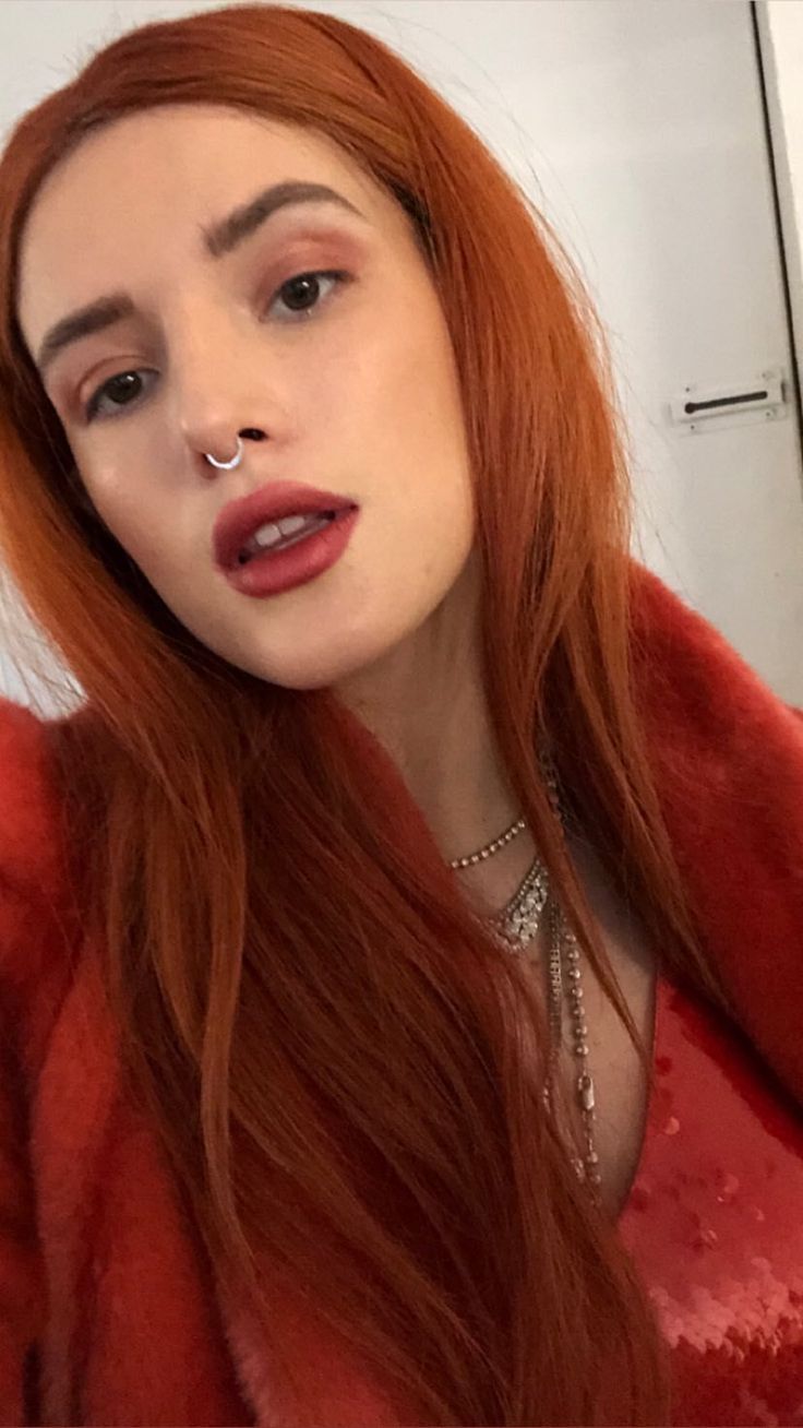 a woman with long red hair and piercings on her nose is taking a selfie