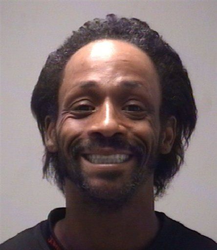 a man with dreadlocks smiles at the camera while wearing a black t - shirt