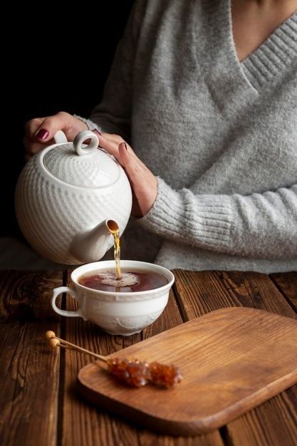 a woman pours tea into a cup on a wooden table next to a cutting board