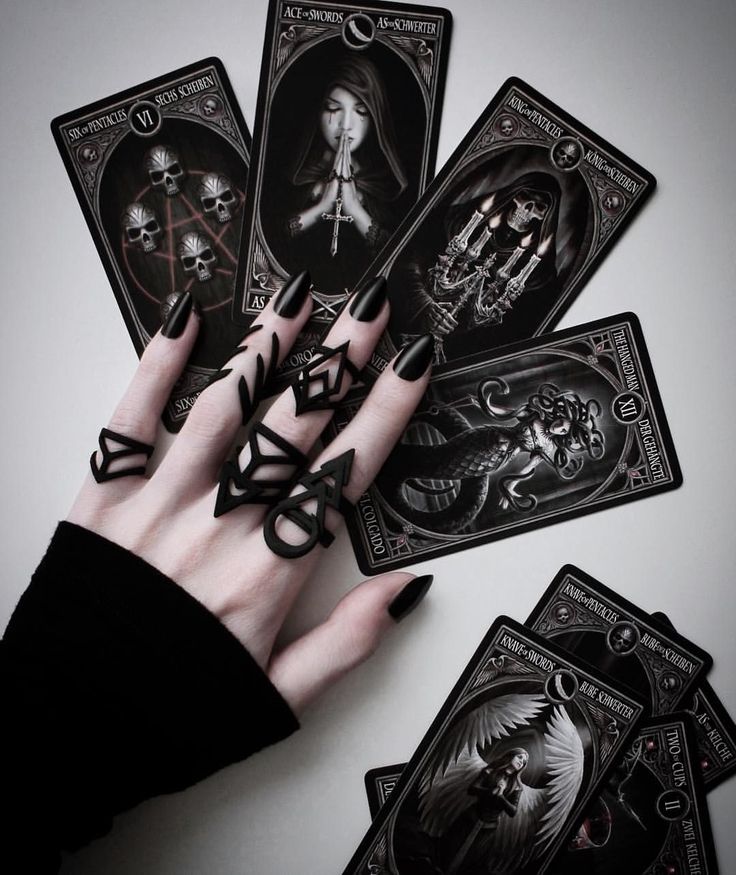 a woman's hand with black nail polish holding five playing cards in front of her