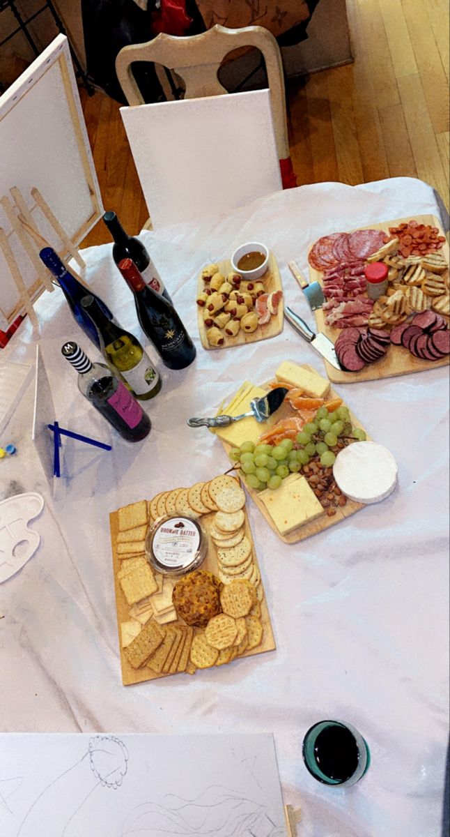 a table topped with lots of different types of cheese and crackers next to bottles of wine