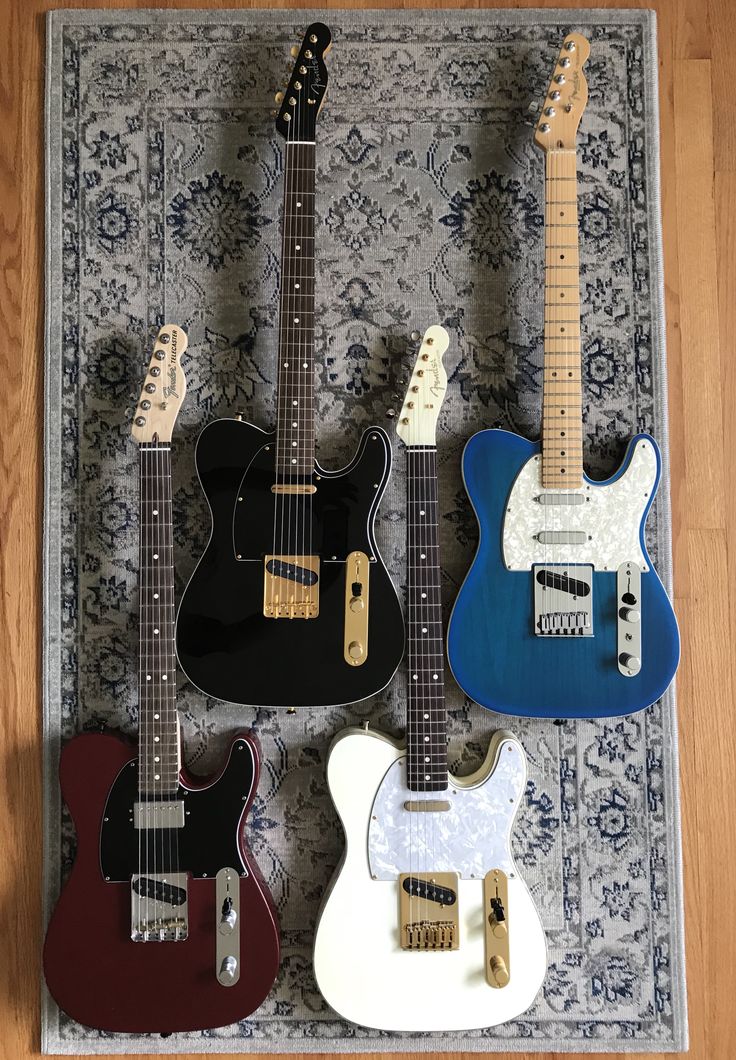 four guitars are lined up in a row on a rug, one is red, one is blue and the other is white