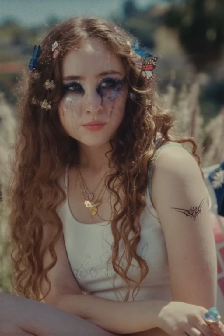 a woman with long hair sitting on the ground wearing sunglasses and a flower in her hair