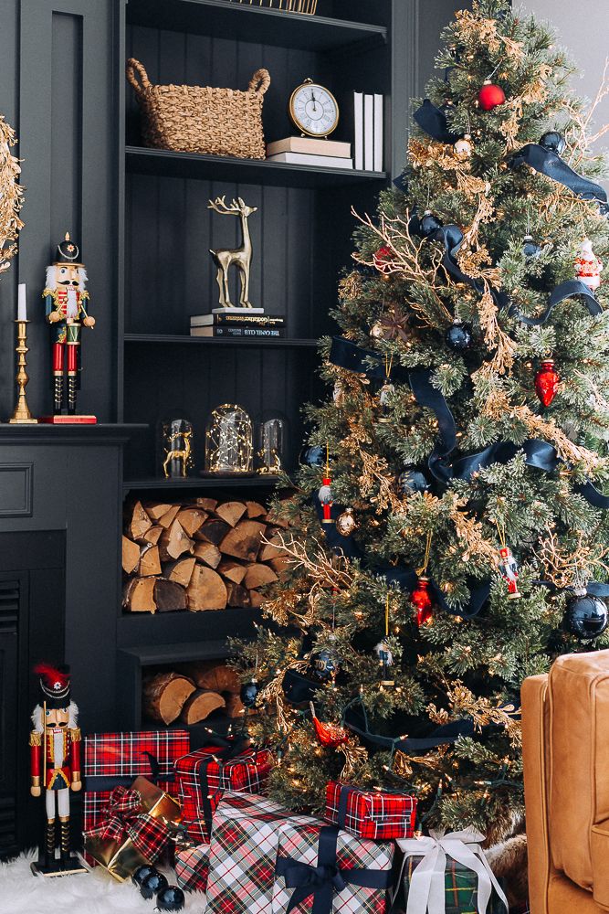 a christmas tree is decorated with red, black and gold ornaments in front of a fireplace