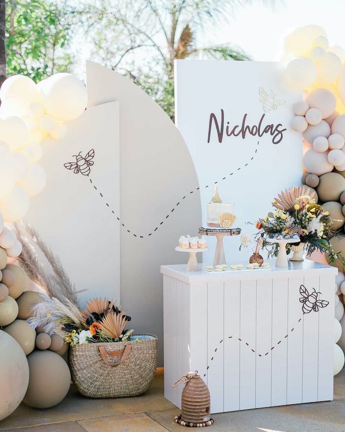 an outdoor dessert table with balloons and decorations on the wall behind it is a sign that says nicholas