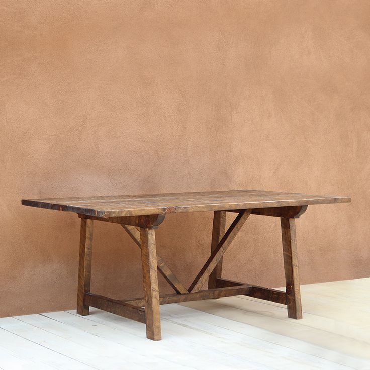 a wooden table sitting on top of a white floor next to a brown stucco wall