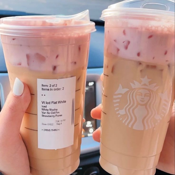 two cups of iced coffee are being held by someone's hand in the car